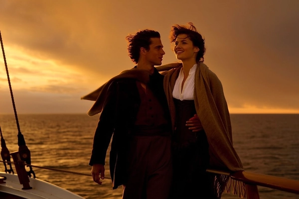Bathed in the warm glow of a golden sunset, a young couple frozen in a timeless embrace stands at the edge of a ship's bow. The man’s dark, classic coat contrasts with the woman's flowing shawl that catches the breeze, unfurling behind her like whispers of a bygone era. Her white blouse peeks softly beneath a tailored dark corset, her expression radiant and hopeful, eyes gazing into the horizon. He holds her close, a protective yet gentle presence, as if shielding her from the vast unknown. The sky’s deep amber hues cascade across their faces, lending a soft, naturalistic warmth that highlights the textured fabrics and delicate movement of the shawl’s fringed edges. The composition centers on their intertwined figures with a subtle shallow depth, where fading light blurs the distant waves into a painterly backdrop. This moment feels both intimate and expansive, a lyrical blend of adventure and burgeoning love, evoking a muted, nostalgic cinematic gloss.