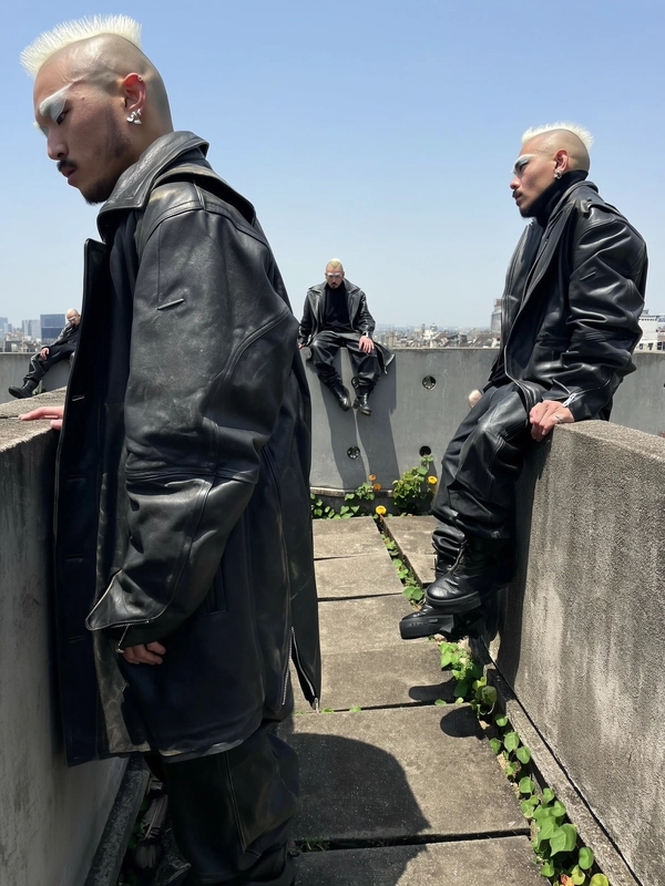 A surreal, candid iPhone photograph showcasing multiple duplicates of the same man scattered across a rugged rooftop garden. He wears heavy layered black leather clothing—thick jackets, pants, and combat boots—his tall platinum mohawk sharply styled and bleached eyebrows visible above. The figures interact subtly, some leaning against raw concrete partitions while others fade partially into shadows or the open sky background, evoking ghostlike qualities. Natural daylight casts crisp, authentic shadows and highlights the detailed textures of his leather layers, hair strands, and skin imperfections. The brutalist concrete environment contrasts with the dynamic presence of the repeating man in various casual, minimally posed stances. The composition uses unexpected cropping and varying scales—from close-up partial profiles to smaller distant silhouettes—enhancing surreal repetition and spatial depth, all captured with the spontaneous authenticity and soft natural light typical of iPhone photography.