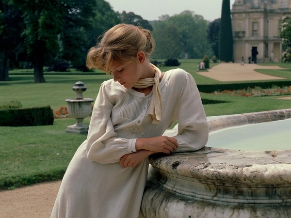 In a serene, sun-dappled garden of a vast estate, a young teenager dressed in a delicate ivory linen dress with subtle embroidery leans thoughtfully against the weathered surface of an ancient marble fountain. Her soft, caramel-toned hair is gently tousled in an effortless style, and a light silk scarf drapes loosely around her neck, catching the afternoon light with a whisper of sheen. The subdued pastel palette of creamyBeige and soft greys blends harmoniously with the lush greenery, evoking an air of contemplative innocence and quiet grace. Under the calm lens of a 50mm prime, the scene is imbued with the tactile texture of linen, smooth marble, and the gentle analog imperfections of 35mm film, reminiscent of classic Slim Aarons’ portraits that celebrate elegant youth and natural poise.