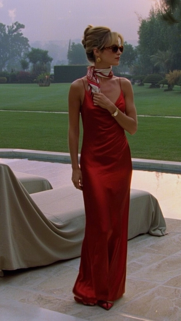 In the soft glow of a fading afternoon, a woman draped in a sumptuous red silk dress stands with quiet poise on the polished marble terrace of a sprawling estate. Her hair, styled in a restrained yet sophisticated updo, complements the understated glamour of oversized tortoiseshell sunglasses perched just so atop her nose. The rich crimson fabric glimmers subtly in the delicate diffused light, its smooth texture contrasting with the coarse weave of the nearby linen-covered chaise longue. Her serene, contemplative gaze drifts toward distant gardens, while a gently knotted Hermès silk scarf adds an air of effortless elegance. Encased in a balanced composition framed through a 50mm lens, the scene exudes the tactile intimacy of analog film—visible 35mm grain softening edges, cream-toned highlights merging with deep, muted shadows reminiscent of Kodachrome. This evocative moment channels the quiet luxury and languid confidence characteristic of early 1980s Slim Aarons imagery. —late-70s / early-80s cinematic photograph, authentic film grain.