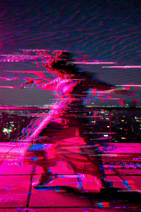 A woman dances on a neon-pink lit urban rooftop at night, her fluid silhouette multiplied through jittered frame skips that create overlapping ghost images shifting in fragmented choreography. Soft digital shadows ripple outward in pixelated waves, blooming into erratic glitch patterns reminiscent of light leaks and corrupted analog film. Her form twists and dissolves into abstract shards of warm magenta, rose, and electric pink hues, interspersed with horizontal scan-line distortions and subtle RGB color separations that flicker like a malfunctioning CRT screen. The composition tightly crops her mid-motion figure, emphasizing the fractured edges and layered overlapping images against a grainy, textured backdrop hinting at distant blurry city lights. A moiré pattern hums faintly across the surface, blending organic human movement with synthetic digital disruption. This fusion of expressive motion and glitch art evokes fleeting memory, ephemeral existence, and nostalgic technological decay under a cyberpunk-inspired pink glow.